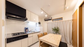 A compact kitchen with a stove, microwave, and sink. There is a dining table with chairs and a potted plant. - UI HOUSE@Minamihorie (1 building rental / 2 stations 4 min. to Namba / walking distance to Kyocera Dome) (大阪市)