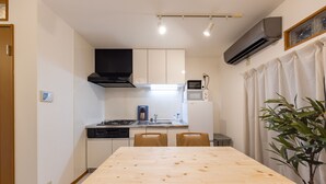 A compact kitchen with white cabinets, a black range hood, a microwave, and a dishwasher. There is a wooden dining table with four chairs. - UI HOUSE@Minamihorie (1 building rental / 2 stations 4 min. to Namba / walking distance to Kyocera Dome) (大阪市)