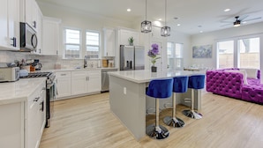 A modern kitchen with white cabinetry, a central island with bar stools, a purple sofa, and a ceiling fan. - Prime EADO 4 BR Downtown Houston  (Houston)