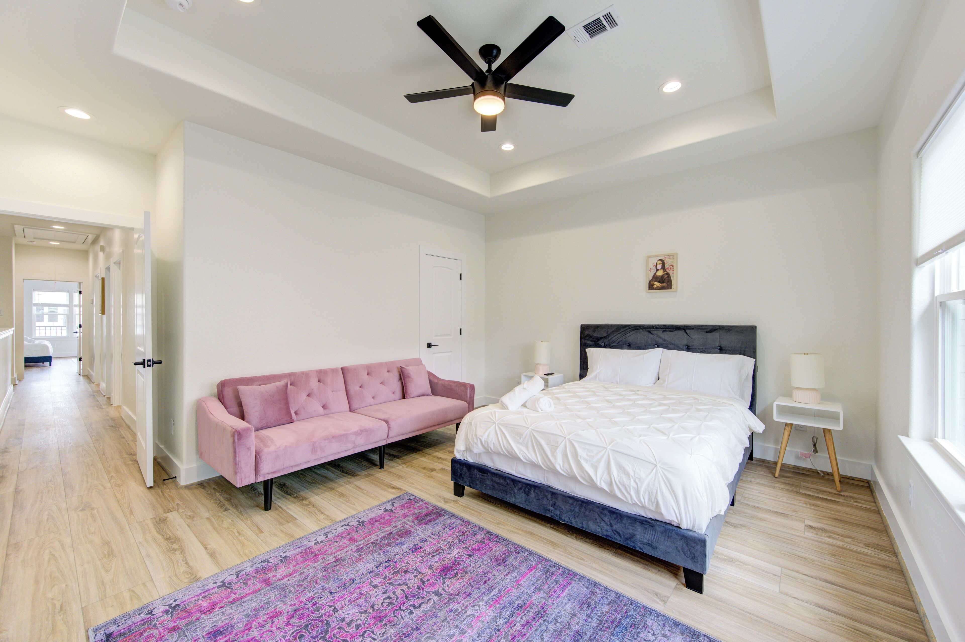 Un dormitorio con una cama, un sofá rosa, un ventilador de techo y un ventanal grande.
