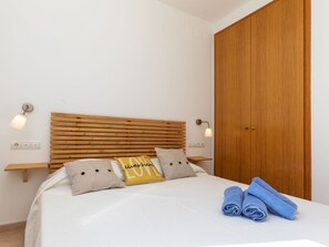 Una cama bien hecha con cabecera de madera, dos lámparas de noche y una toalla doblada sobre la cama.