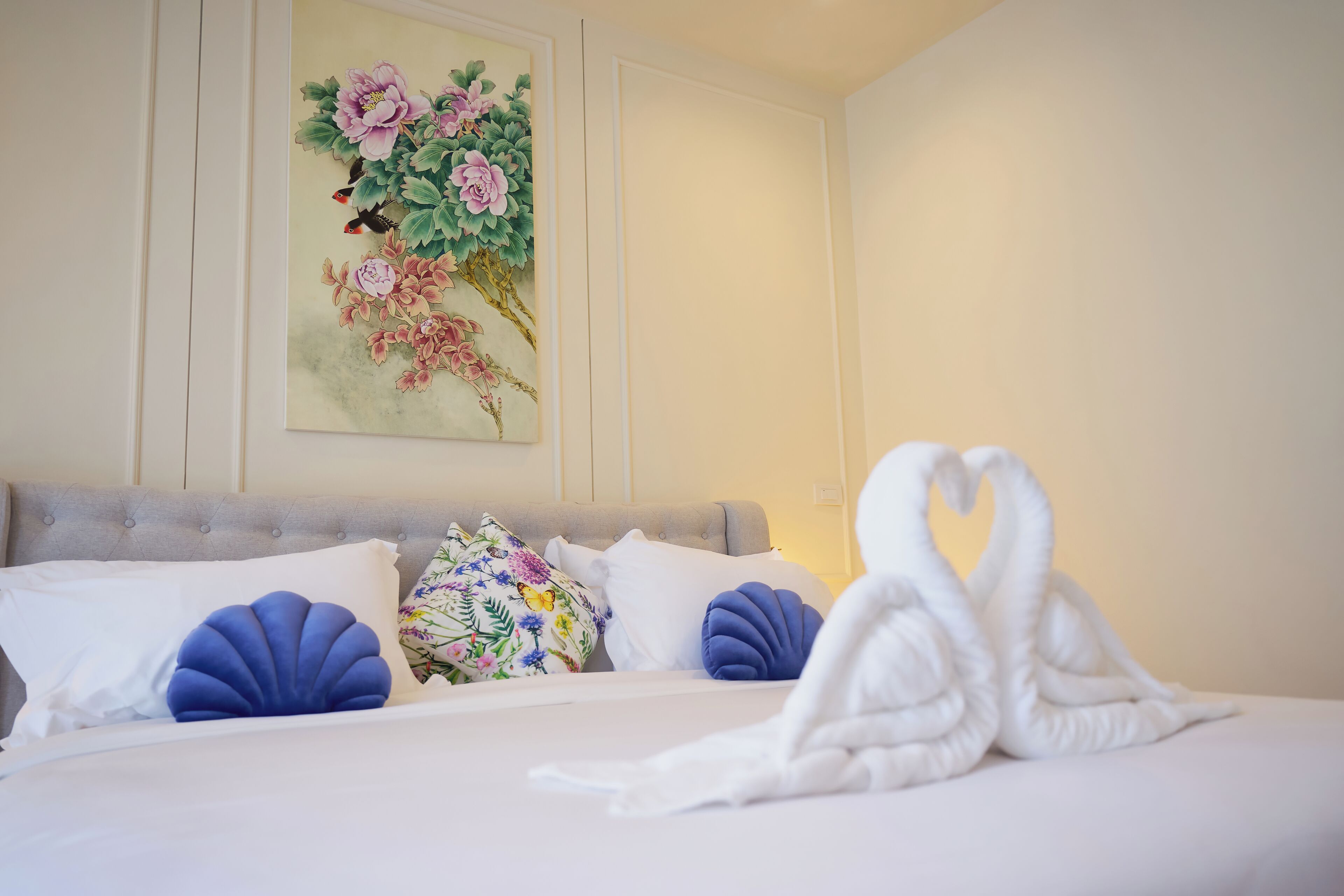Un lit bien fait, avec du linge de lit blanc, un tableau décoratif représentant des fleurs accroché au mur et une serviette en forme de cygne posée sur le lit.