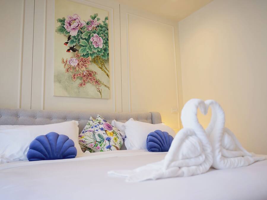 A neatly made bed with white linens, a decorative painting of flowers on the wall, and a swan-shaped towel on the bed.
