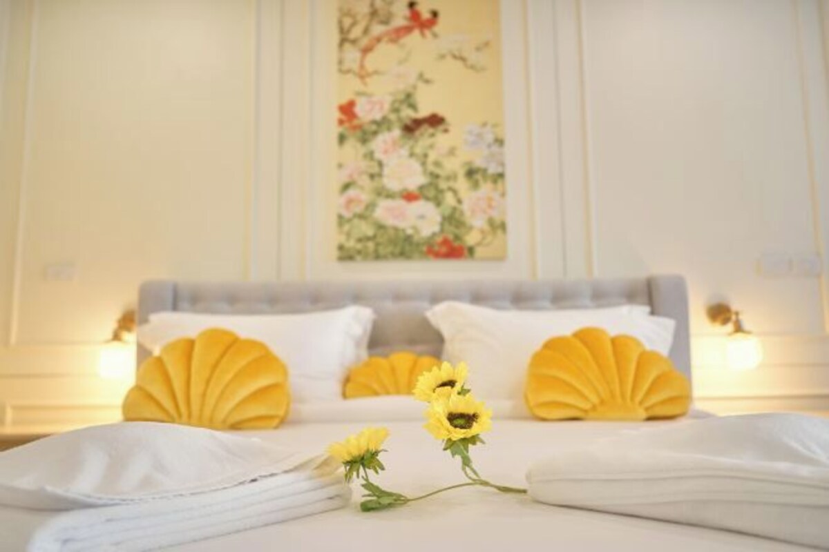 A hotel room with a bed, pillows, and a painting on the wall.