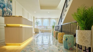 Un hall de hotel con mostrador de recepción, baldosas de diseño, una escalera y plantas en macetas.