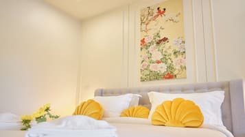 Una cama bien hecha con almohadas blancas y amarillas, una obra de arte floral en la pared y un ramo de flores amarillas.