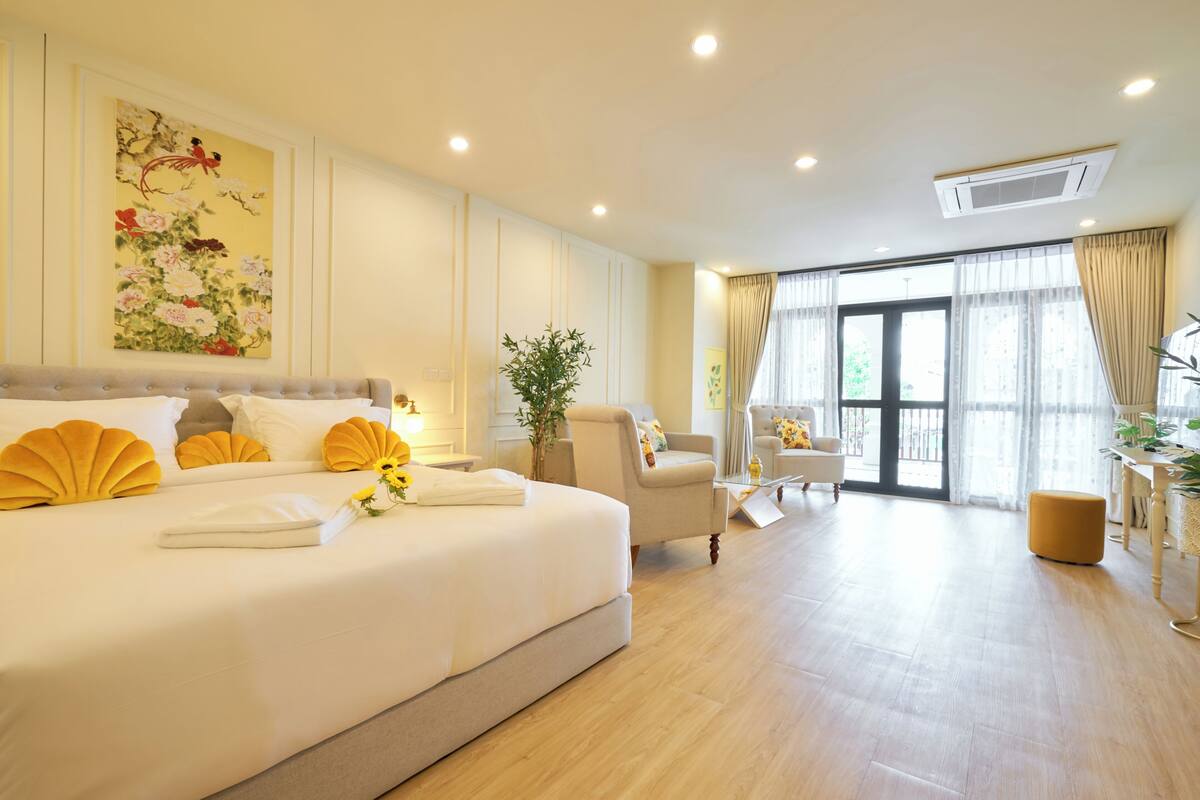 Habitación de hotel con una cama grande, un área de descanso con una silla y una mesa, y vistas a través de un ventanal.