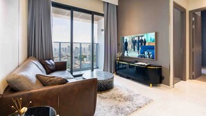 A modern living room with a leather sofa, a round coffee table, a flat-screen TV on a black stand, and a large window with a city view. - Kotrip MarQ Paradise Vacation (Ho Chi Minh City)