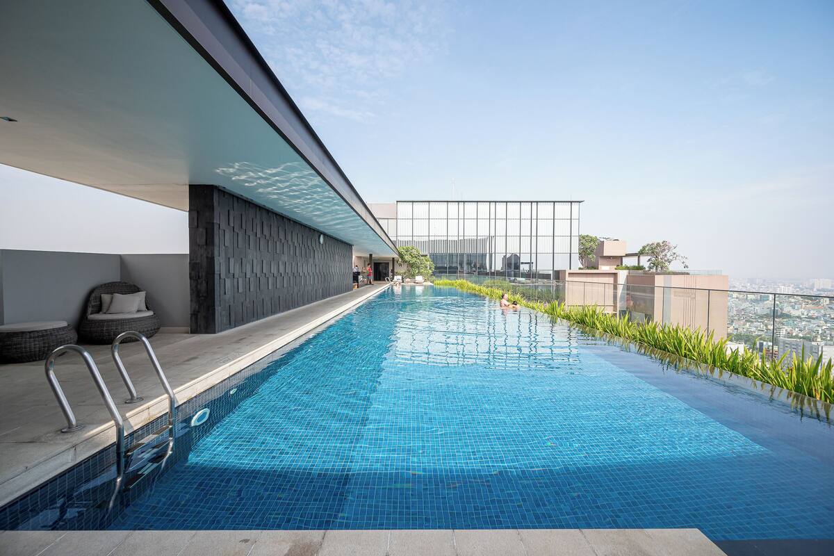 A rooftop infinity pool with a city view, a seating area with cushions, and a glass railing.