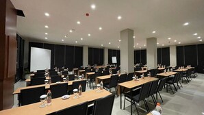 A conference room with multiple tables, chairs, and a projection screen. - Horison Resort Dieng (Kejajar)