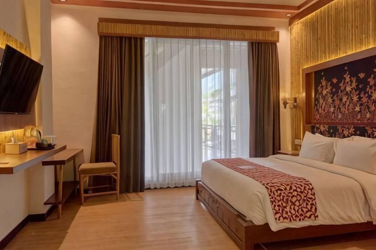 A hotel room with a bed, a desk, a chair, a TV, and a large window with curtains.