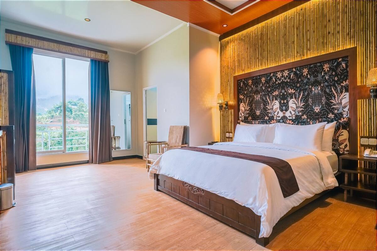 A spacious bedroom with a large bed, a view of the outdoors, and a decorative headboard.