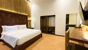 A hotel room with a large bed, a wooden headboard, a built-in wardrobe, a desk with a mirror, and a television mounted on the wall. - Horison Resort Dieng (Kejajar)