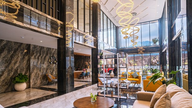 A spacious lobby with marble walls, a seating area with sofas and chairs, a coffee table, and a view of the outdoors through large windows. - Horison Resort Dieng (Kejajar)