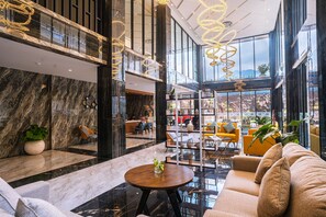Eine geräumige Lobby mit Marmorwänden, einer Sitzecke mit Sofas und Sesseln, einem Couchtisch und Blick ins Freie durch große Fenster.