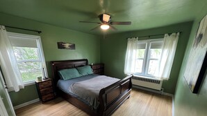 Ein Schlafzimmer mit einem hölzernen Bett, grünen Wänden, einem Deckenventilator und einem Fenster mit weißen Vorhängen.