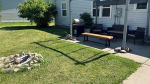 Ein Garten mit einer Holzbank, einem Grill und einer Pergola.