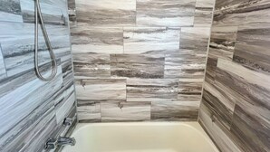 Ein Badezimmer mit Dusche, Badewanne und einer Wand mit Holzoptik-Fliesen.