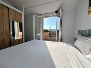 Ein Schlafzimmer mit einem Bett, einem Holzschrank und einer Glastür, die zu einem Außenbereich mit Tisch und Stühlen führt.
