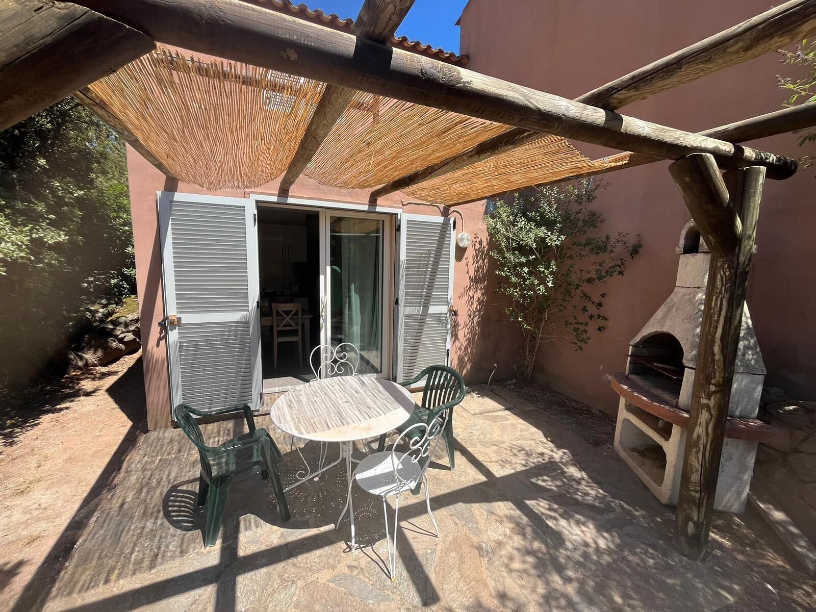 Une terrasse extérieure avec une table et des chaises, une pergola en bois et un four en pierre.