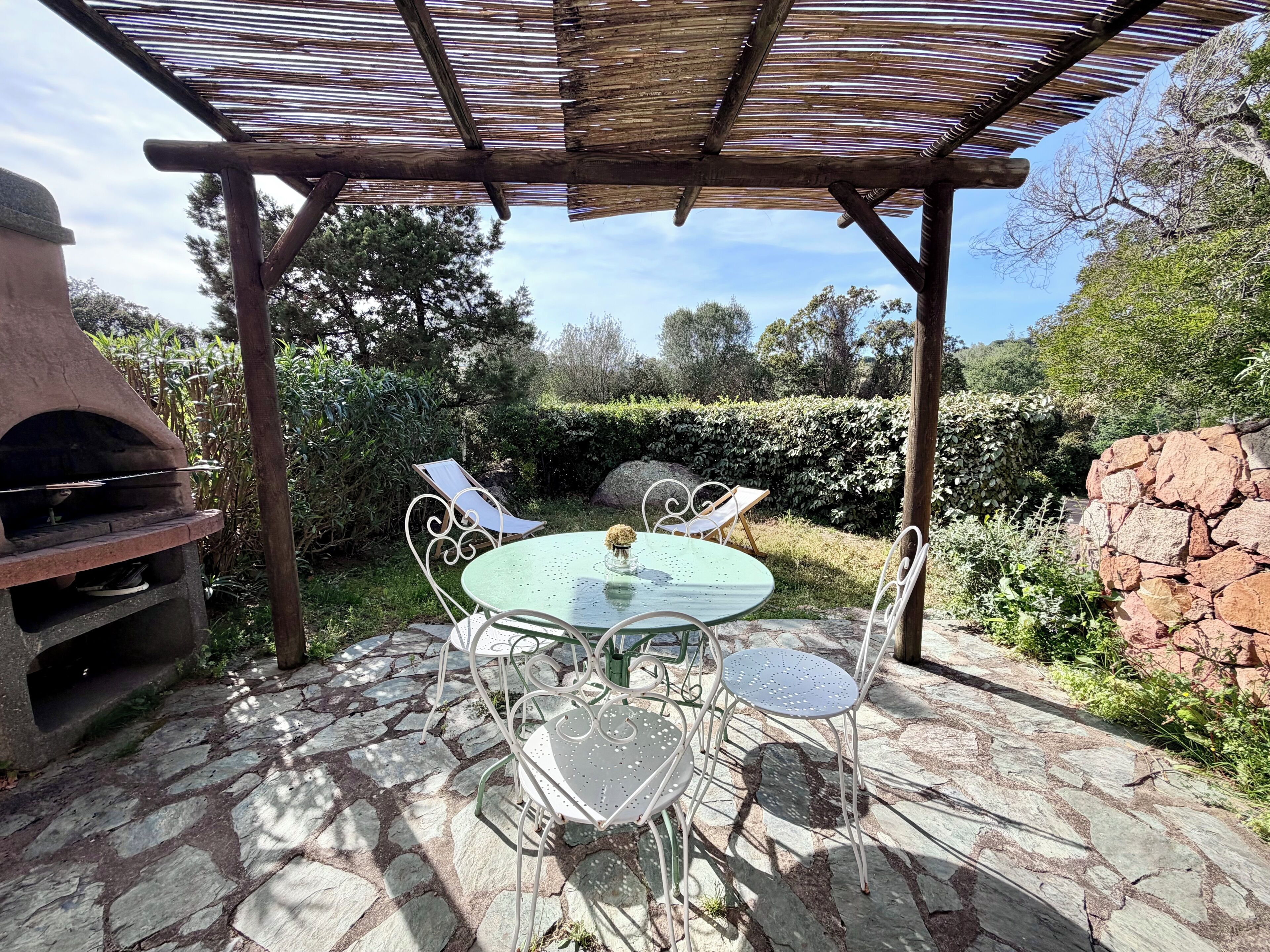 A stone patio with a round table and four chairs, a barbecue grill, and a pergola structure.