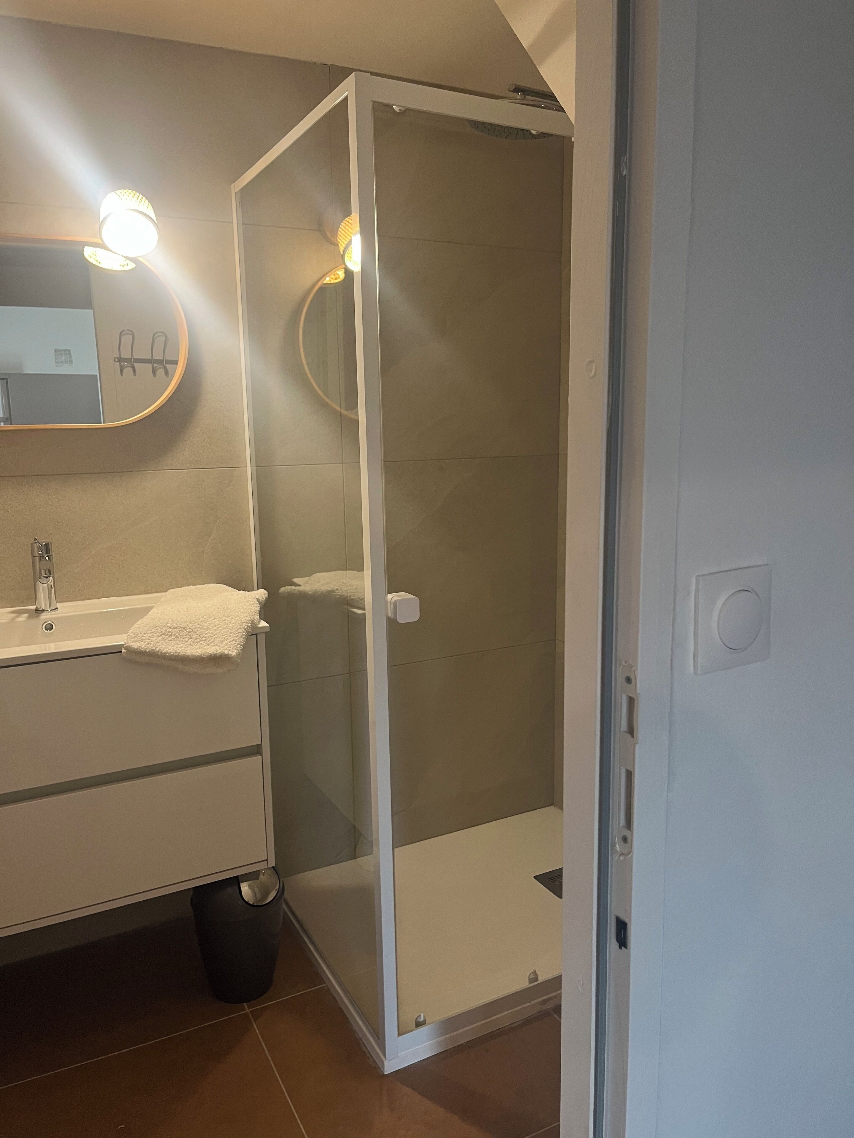 A bathroom with a glass-enclosed shower, a sink with a towel, and a mirror with lights.