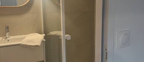 Ein Badezimmer mit Duschkabine, Waschbecken mit Handtuch und Spiegel mit Beleuchtung.