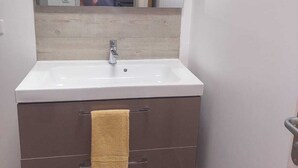 Une salle de bain avec un lavabo blanc, un miroir et une serviette accrochée à la porte.