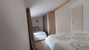Un couloir étroit mène à une chambre qui contient un lit, une porte et une petite chaise blanche.
