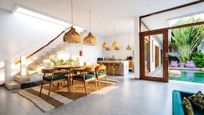 Una cocina moderna con una isla central, un comedor con mesa y sillas de madera, y una escalera de diseño único.
