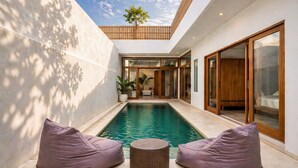 Un área de piscina interior moderna con vista despejada al cielo, cerca de una valla de madera y una gran puerta corrediza de vidrio que da a un espacio de estar.