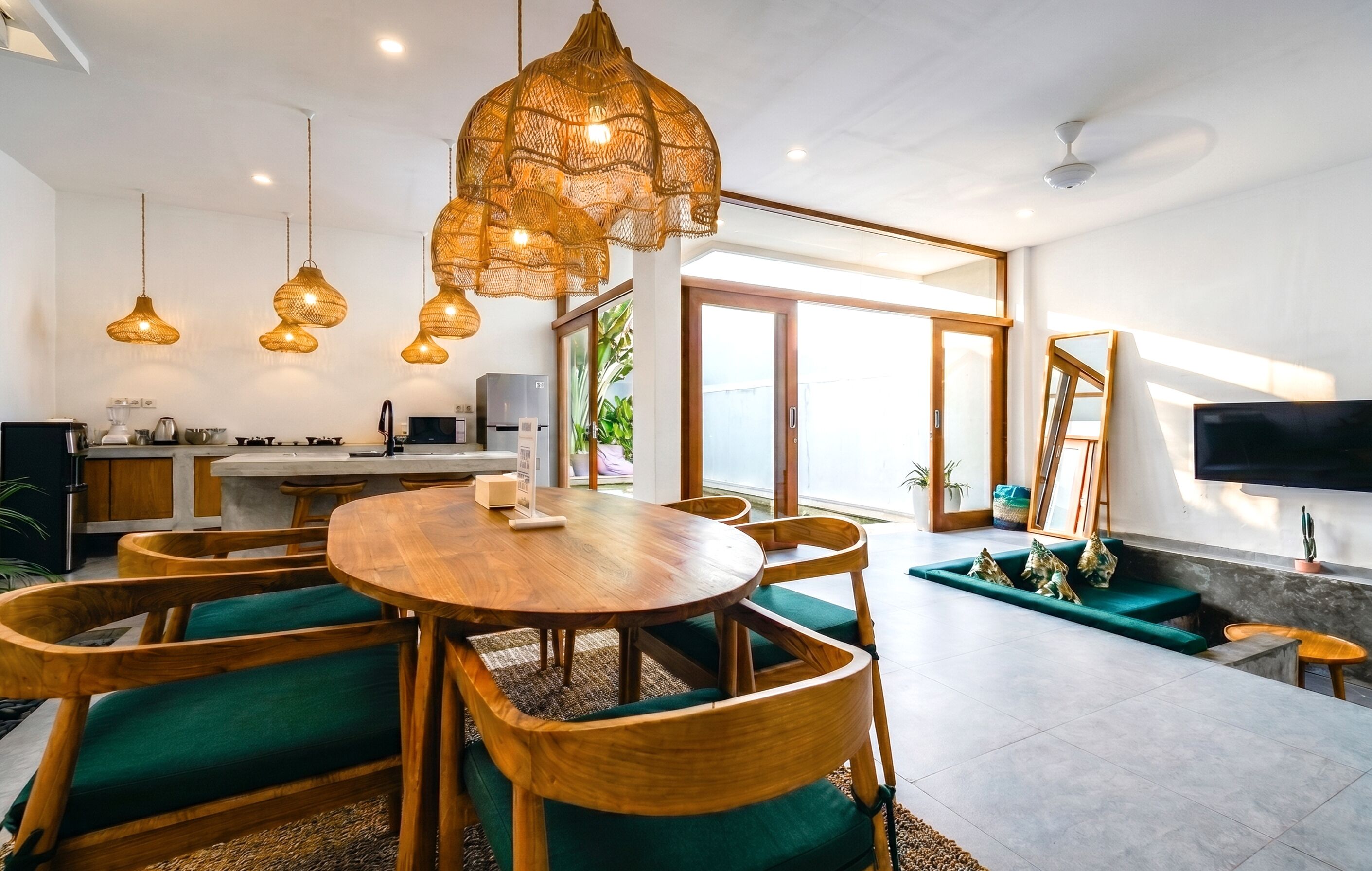 A modern kitchen with wooden cabinets, a dining table with chairs, and hanging wicker pendant lights.