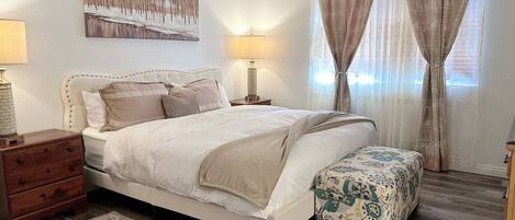 A bedroom with a bed, bedside tables, a nightstand, a patterned rug, and a window with curtains.