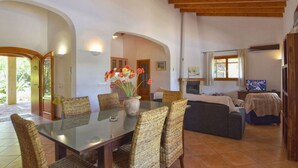 A spacious living area with a glass-top dining table surrounded by wicker chairs, a fireplace, and a television.
