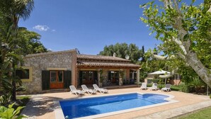 A stone house with a swimming pool, outdoor seating, and lush greenery.
