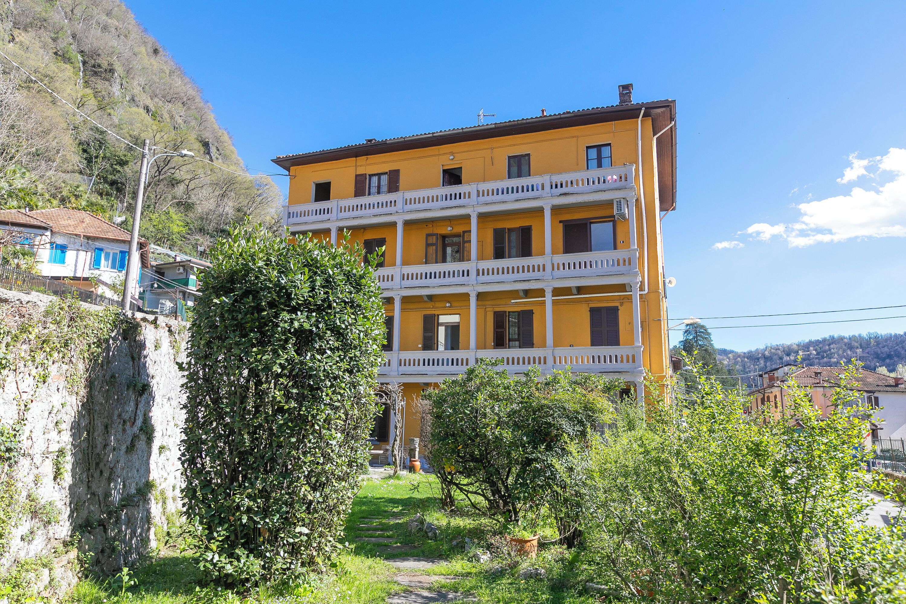 A multi-story yellow building with balconies, surrounded by greenery and a hillside.