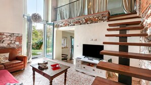 A living room with a stone fireplace, a television, a wooden coffee table, and a leather sofa. - La Maison Du Lac - 50 Meters From Lake , Private Parking&bbq (Monvalle)