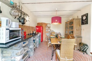A kitchen with a stone wall, a red refrigerator, a microwave, and a dining area with wicker chairs.