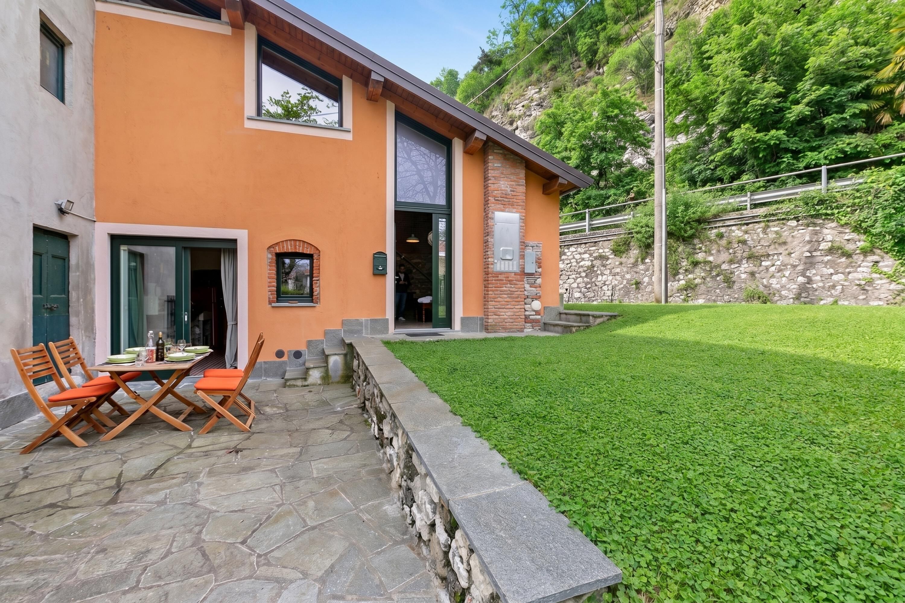 Un bâtiment moderne doté d’une terrasse en pierre, d’un espace extérieur aménagé pour s’asseoir et d’une pelouse bien entretenue.