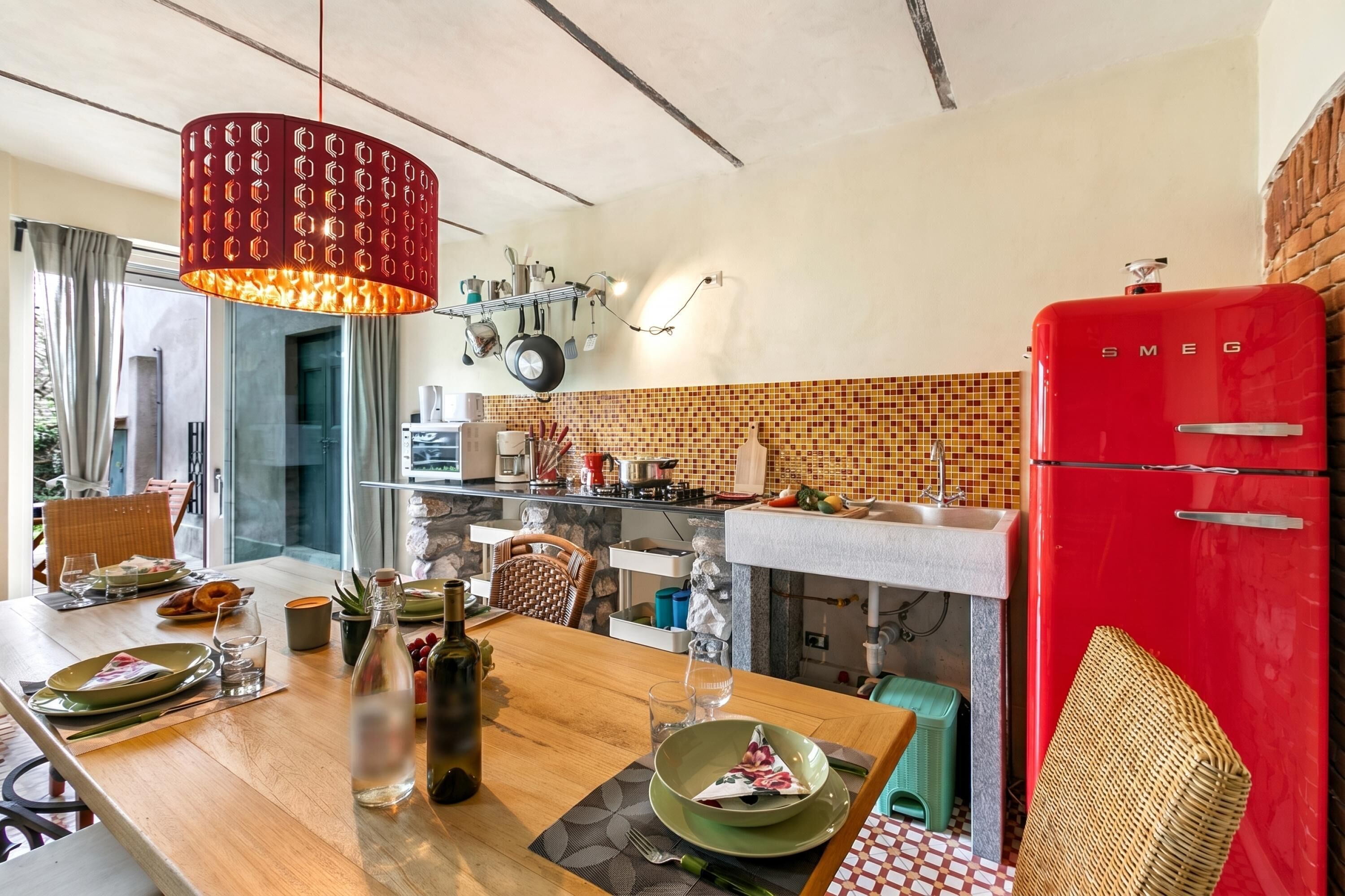 Una cocina con un refrigerador rojo, ollas colgadas y una mesa de comedor con platos y vasos.