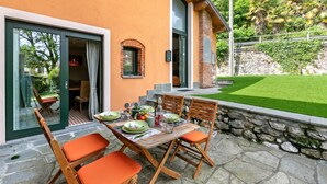 An outdoor dining area with a table set for four, stone steps leading to a door, and a well-maintained lawn in the background. - La Maison Du Lac - 50 Meters From Lake , Private Parking&bbq (Monvalle)