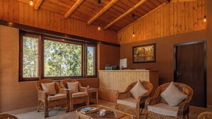 Una habitación con paneles de madera, muebles de mimbre, ventanas amplias y un cuadro en la pared.
