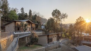 Un hotel moderno con fachada de piedra, varios balcones y vistas a las colinas circundantes.