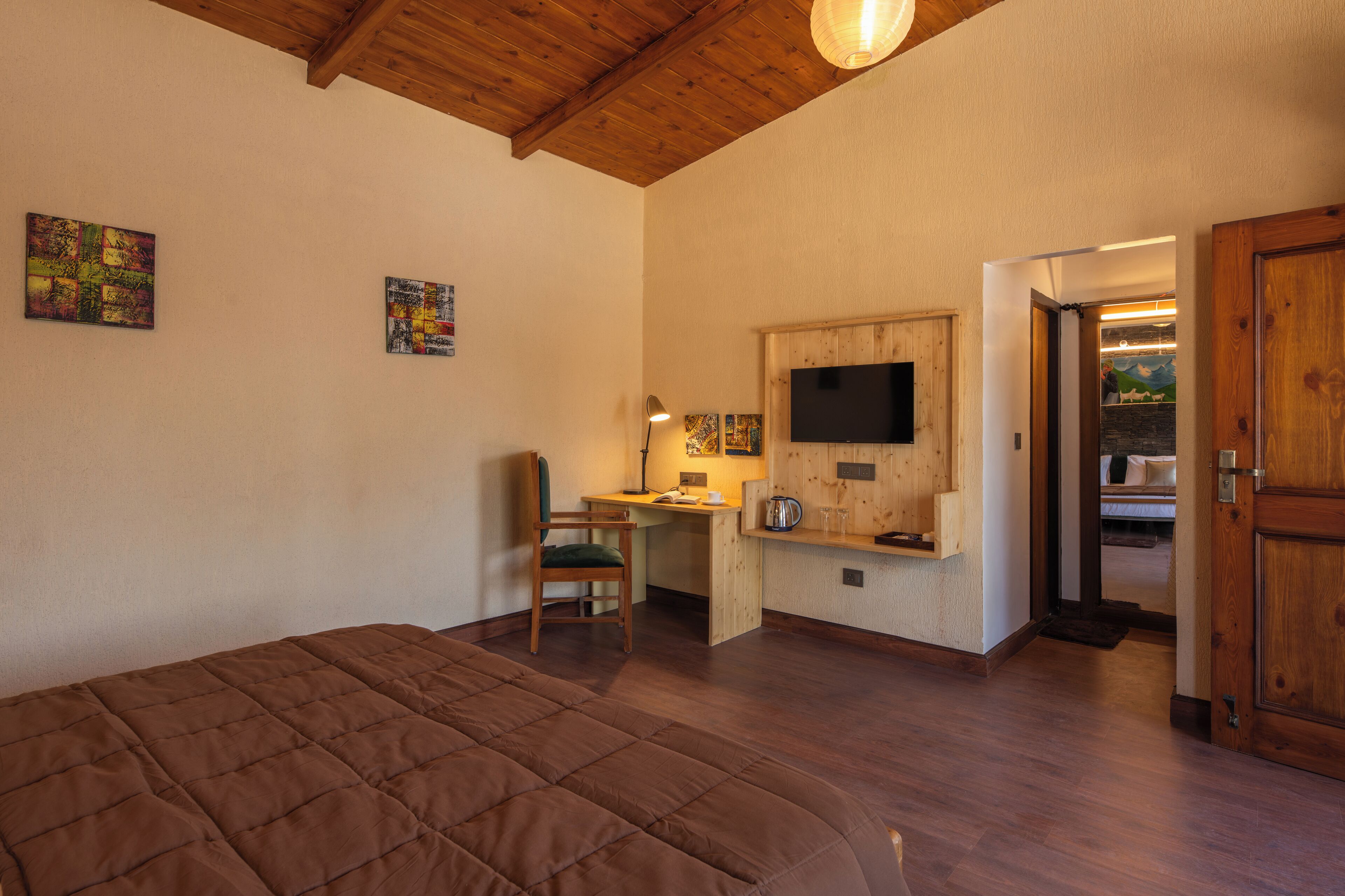 Un dormitorio con cama, escritorio, silla, televisor y obras de arte en la pared.