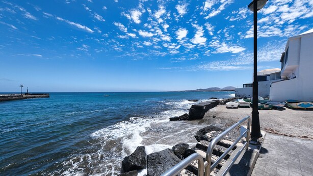 A coastal scene with a rocky shoreline, a metal railing, and a white building with a flat roof.