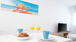A dining area with a table set for breakfast, including croissants and orange juice, and a beach-themed painting on the wall.