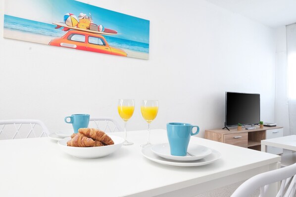 A dining area with a table set for breakfast, including croissants and orange juice, and a beach-themed painting on the wall.