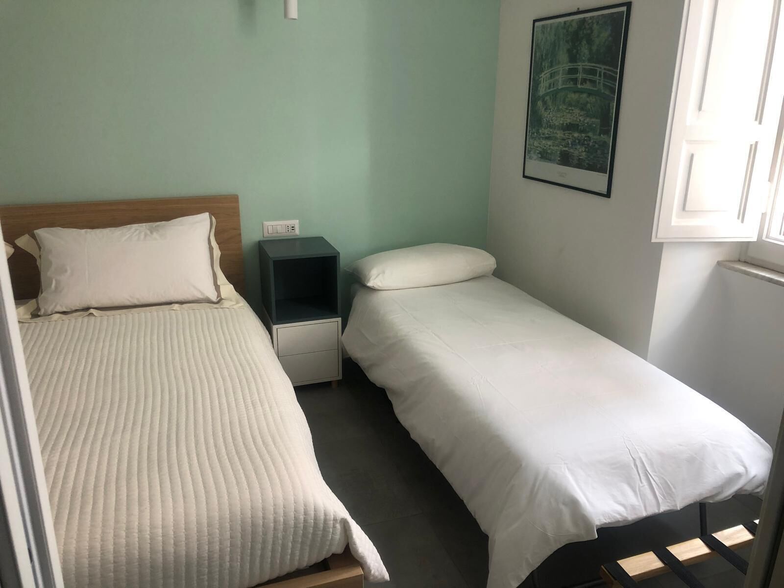 Une chambre avec un grand lit, un lit simple plus petit, une table de chevet et un tableau accroché au mur.