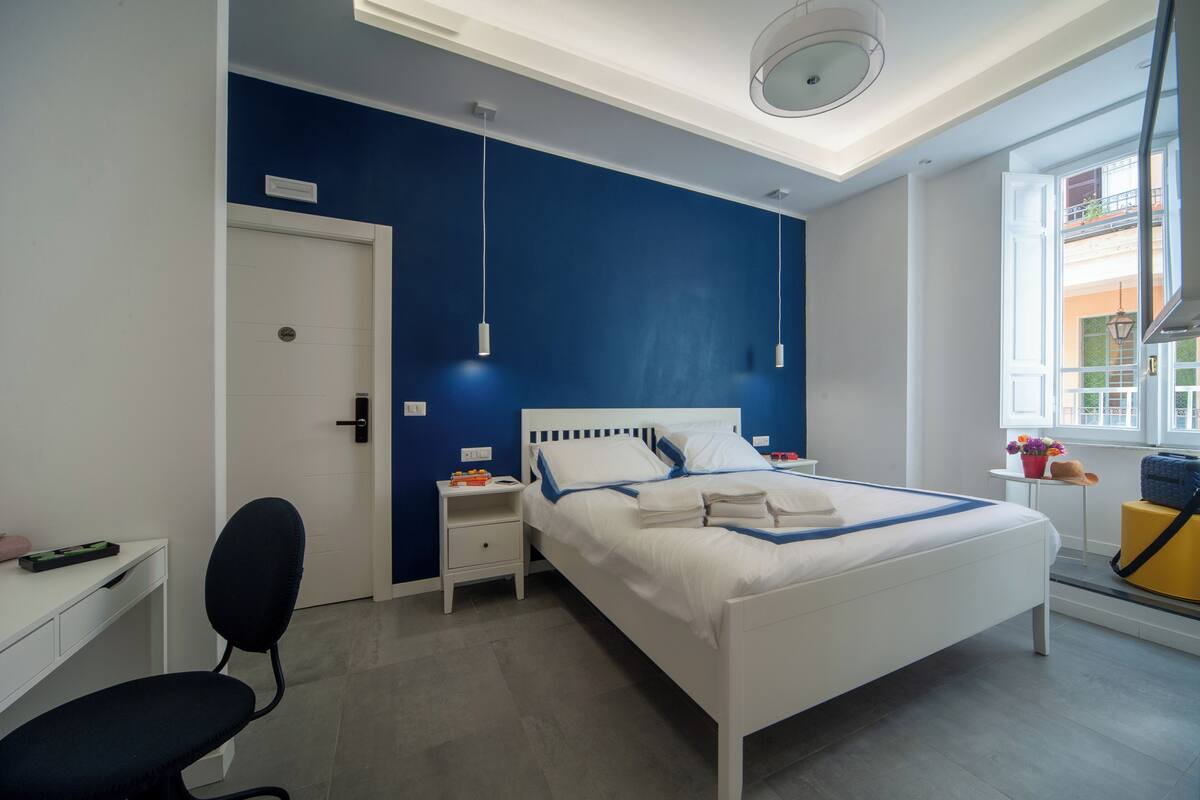 A modern bedroom with a white bed, blue accent walls, a desk, and a chair.