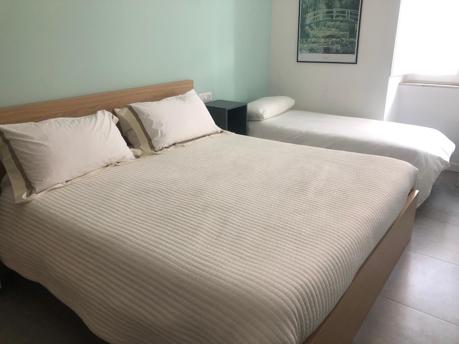 A double bed with a wooden headboard, two bedside tables, and a wall-mounted picture.